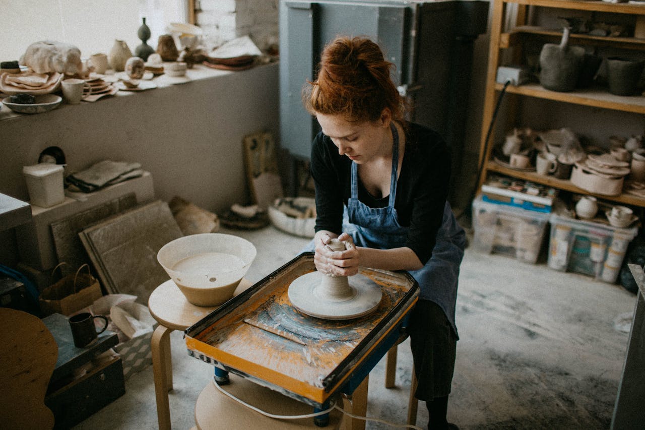 A skilled woman shapes a clay pot in an artistic pottery studio.